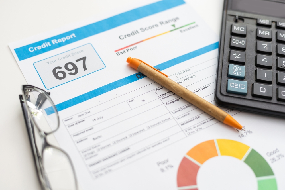 Credit report showing a score of 697 with financial chart, calculator, pen, and eyeglasses on desk.