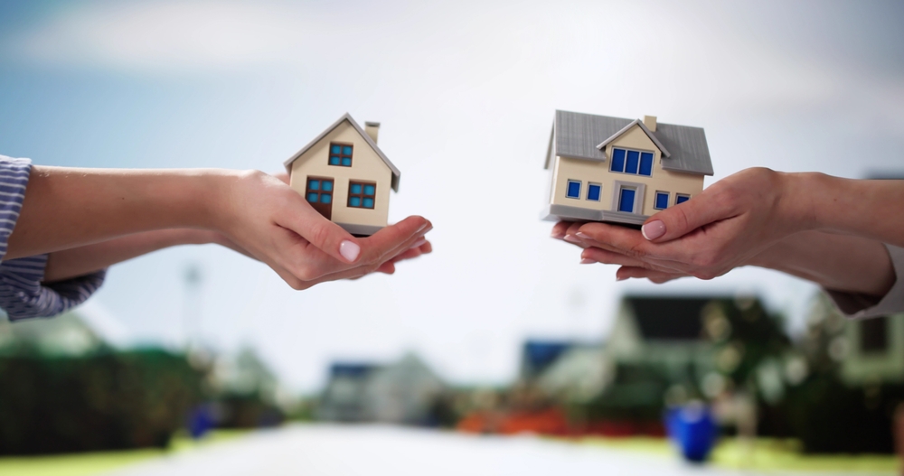 Two hands exchanging miniature house models, symbolizing a 1031 exchange of investment properties for tax deferral.
